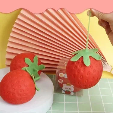 red strawberry-shaped squishy TheMoodease stress balls placed on a pastel surface, cute sensory fidget toys designed for stress relief and relaxation.