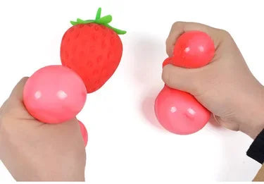 Two hands squeezing pink squishy TheMoodease stress balls with a strawberry-shaped fidget toy in the center, sensory stress relief and hand exercise with soft squeeze toys.