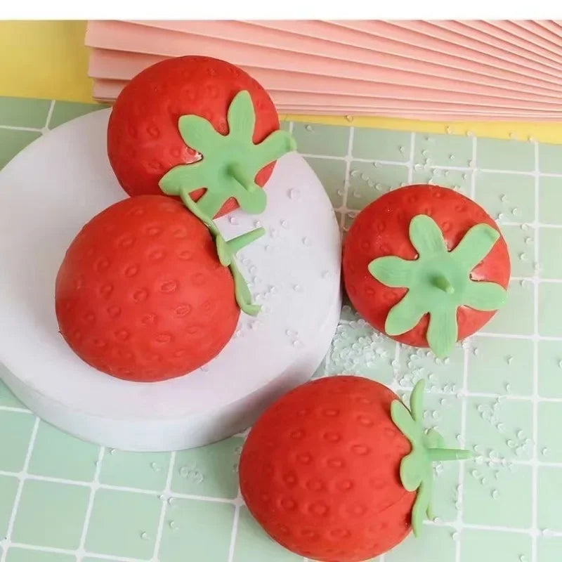 Red strawberry-shaped squishy TheMoodease stress balls placed on a pastel surface, cute sensory fidget toys designed for stress relief and relaxation.